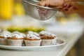 Confectioner sprinkles freshly baked muffins with icing sugar. Sweet pastries, recipes, cooking Royalty Free Stock Photo