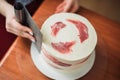 Confectioner using a knife to smooth the sides and top of the cake, close-up top view photo. The confectioner smoothes the white c