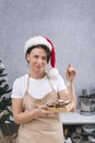 Confectioner woman in New Years hat and kitchen robe holds box of delicious sweets and winks. Vertical frame Royalty Free Stock Photo