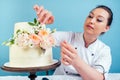 Confectioner woman pastry-cook in confectioner`s jacket decorate appetizing creamy white two-tiered wedding cake with