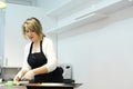 A confectioner works in his workshop. A woman puts dough products from a pastry mat onto a baking sheet