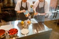 Confectioners in aprons fill fresh bun with cream in modern bakery shop