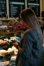 Confectionery customer, client in sweet-shop, pastry-shop. Back view of young woman choosing cake desserts from display