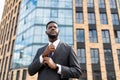 Confident african american businessman adjusting necktie, standing against office center in urban area, free space Royalty Free Stock Photo