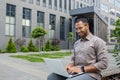 Confident african american businessman using laptop outdoors near modern office building Royalty Free Stock Photo