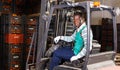 Confident African-American male forklift driver working in citrus fruit warehouse
