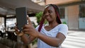 Confident african american woman basking in sunlight, making selfie with touchpad, smiling joyously at urban coffee shop terrace Royalty Free Stock Photo