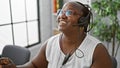 Confident african american woman happily working as a business executive, wearing a headset, and smiling at the office, speaking Royalty Free Stock Photo