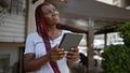 Confident african american woman, radiant with happiness, enjoying her touchpad at a lively coffee shop terrace, basking in the