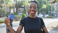 Confident african american woman, radiating happiness, flaunting her credit card on a busy city street, embodying financial