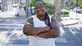 Confident african american woman, sporting braids and glasses, smiling widely and standing with crossed arms on an urban street,