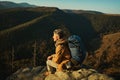 Confident alone man hiker with backpack sitting on stone of cliff and enjoying view of mountain summit Royalty Free Stock Photo