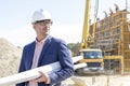 Confident architect holding rolled up blueprints at construction site Royalty Free Stock Photo