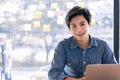 Confident asian business male smiling and look at camera while working on laptop computer at office Royalty Free Stock Photo