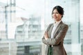A confident Asian businesswoman in a business suit stands with her arms crossed in an office corridor Royalty Free Stock Photo