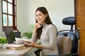 Confident Asian businesswoman at her office desk, hand on chin, daydreaming about success Royalty Free Stock Photo