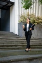 A confident Asian businesswoman is holding a coffee cup and binders while walking down the stairs Royalty Free Stock Photo