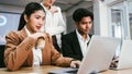 A confident Asian businesswoman holding a coffee cup, sitting and working on a laptop with her colleague with a woman standing. Royalty Free Stock Photo