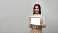 Confident Asian female showing a white tablet screen mockup, standing over grey background Royalty Free Stock Photo