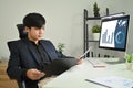 Confident asian male accountant advisor holding open office binder with paperwork while sitting at workstation Royalty Free Stock Photo