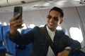 Confident asian male travel blogger leaning on the airline seats and holding camera recording his video vlog Royalty Free Stock Photo