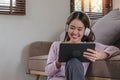 Confident asian woman listening to music with earphones and use tablet while relaxing of work in the office at home. Royalty Free Stock Photo