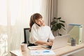 Confident Asian woman talking on her mobile phone and using laptop while sitting at desk and working from home. Home office Royalty Free Stock Photo