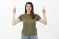 Confident and assertive attractive female student with tattoo in olive t-shirt looking self-assured up as pointing