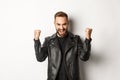 Confident and assertive man in leather jacket making fist pump, rejoicing of winning, feeling encouraged and satisfied