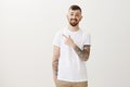 Confident assured handsome bearded guy with cool tattoos on arms, pointing at upper left corner with finger gun gesture Royalty Free Stock Photo