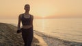 Athletic woman walking beach holding sport mat at sunset. Girl going exercising. Royalty Free Stock Photo