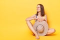 Confident attractive woman wearing striped swimming suit and hat isolated on yellow background sitting looking away at Royalty Free Stock Photo