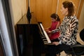 Confident authentic female pianist, music teacher giving an individual piano lesson to her little student. Musical