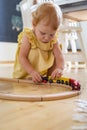 Confident baby girl in dress playing wooden train railways Maria Montessori ecological materials