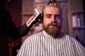 Confident barber mster cuts hair and beard of men in the barbershop