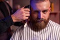 Confident barber mster cuts hair and beard of men in the barbershop