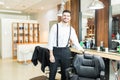 Confident Barber Smiling While Standing By Chair In Shop