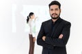 Confident bearded businessman smiling while standing and arms crossed, Businesswoman gives presentation on background, looking at Royalty Free Stock Photo