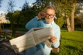 Confident bearded mature man reading daily newspaper on park bench