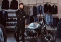 Bearded stylish man dressed in black suit posing with crossed arms near retro sports motorbike at the men`s clothing Royalty Free Stock Photo