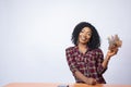 Confident and beautiful young black woman sitting and holding money, in front of a white background