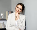 Confident beautiful young woman in a beige jacket looking at the camera leaning against a gray wall Royalty Free Stock Photo