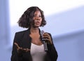 Confident black African American business woman with microphone speaking in auditorium at corporate event or seminar giving Royalty Free Stock Photo