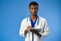 Confident black doctor posing over blue studio background. Royalty Free Stock Photo