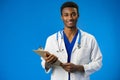 Confident black doctor posing over blue studio background. Royalty Free Stock Photo