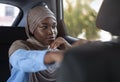 Confident black muslim businesswoman sitting in car and looking through window