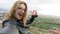 Confident Blond Lady taking a picture with her camera in a viewpoint. Teenager in glasses with short hair smiling showing teeth Royalty Free Stock Photo