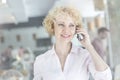 Confident blond mature owner talking on smartphone at restaurant