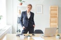 Confident business expert. Attractive businesswoman in smart black wear looking at camera while standing near her desk in creative Royalty Free Stock Photo