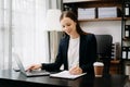 Confident business expert attractive smiling young woman typing laptop ang holding digital tablet on desk in office Royalty Free Stock Photo